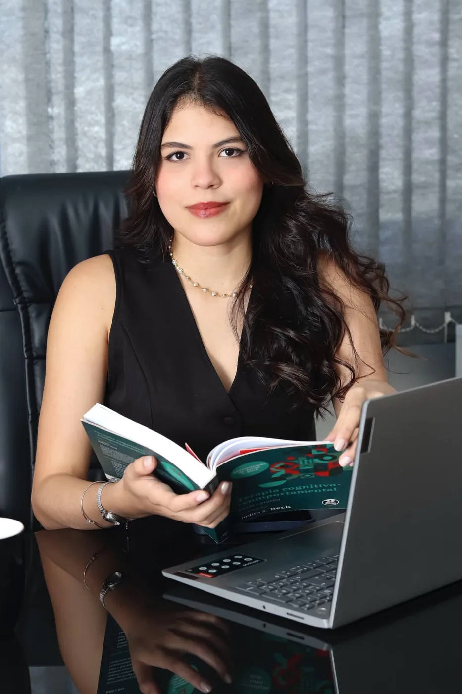 Rayssa Aguiar sentada à mesa de trabalho, com livro de psicologia nas mãos